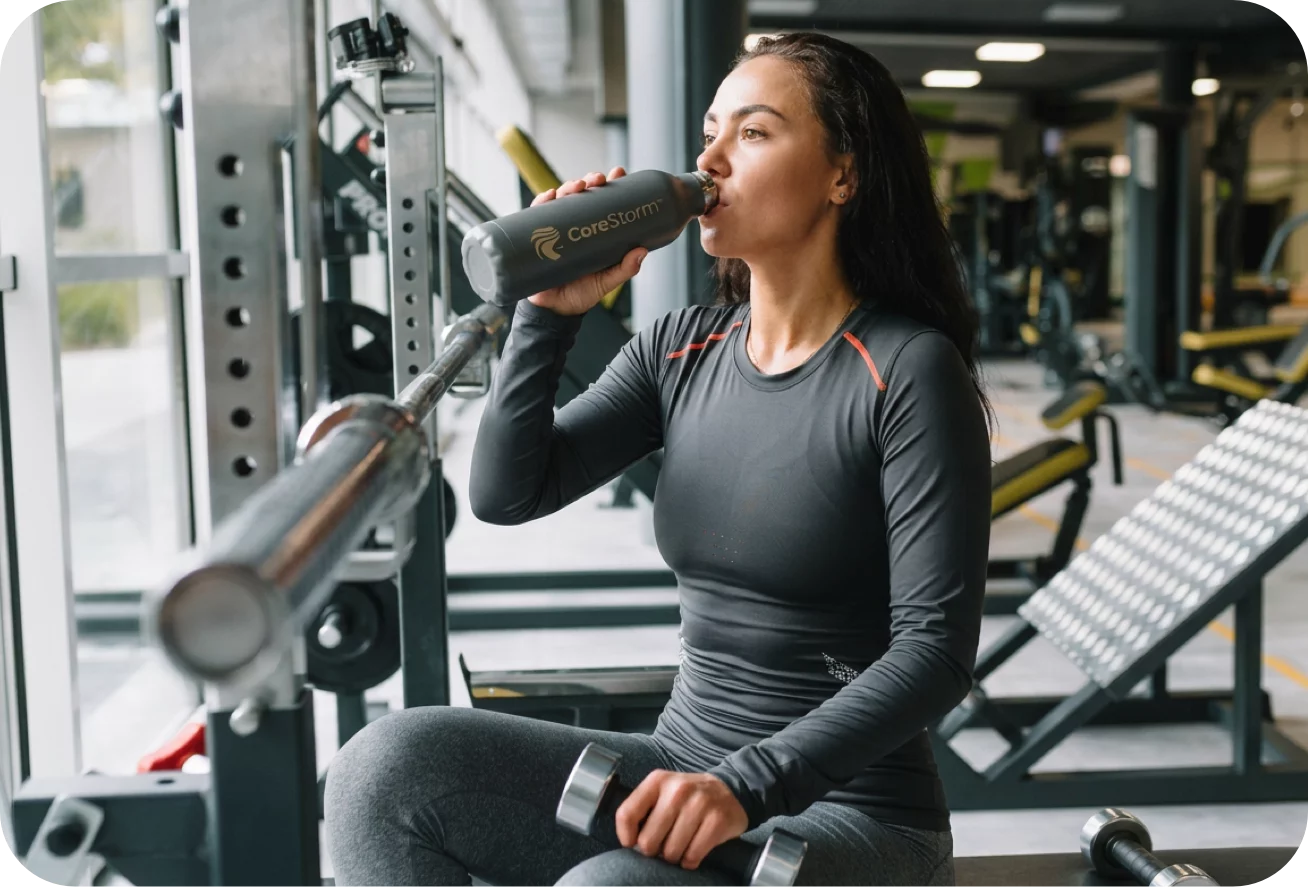 Woman drinking from a water bottle in a gym setting