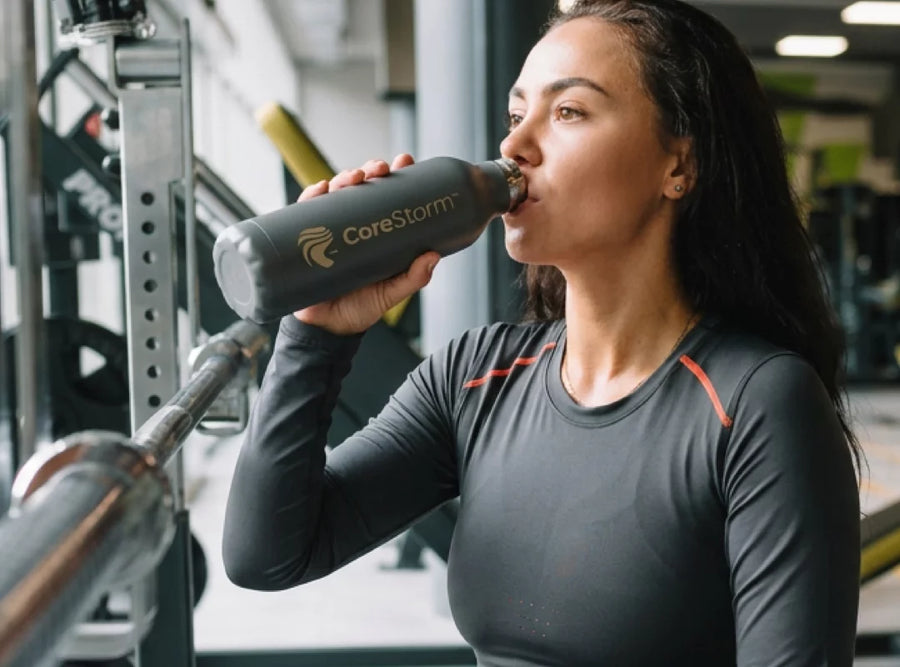 Woman drinking from a CoreStorm water bottle in a gym setting