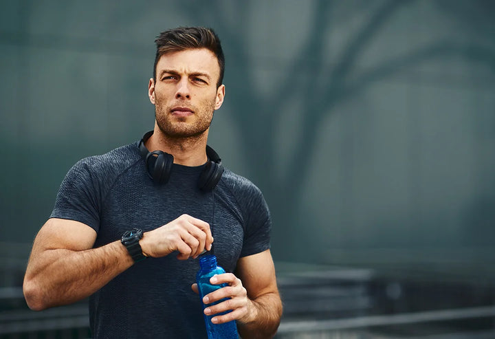 Man in athletic wear holding a blue water bottle against a dark background